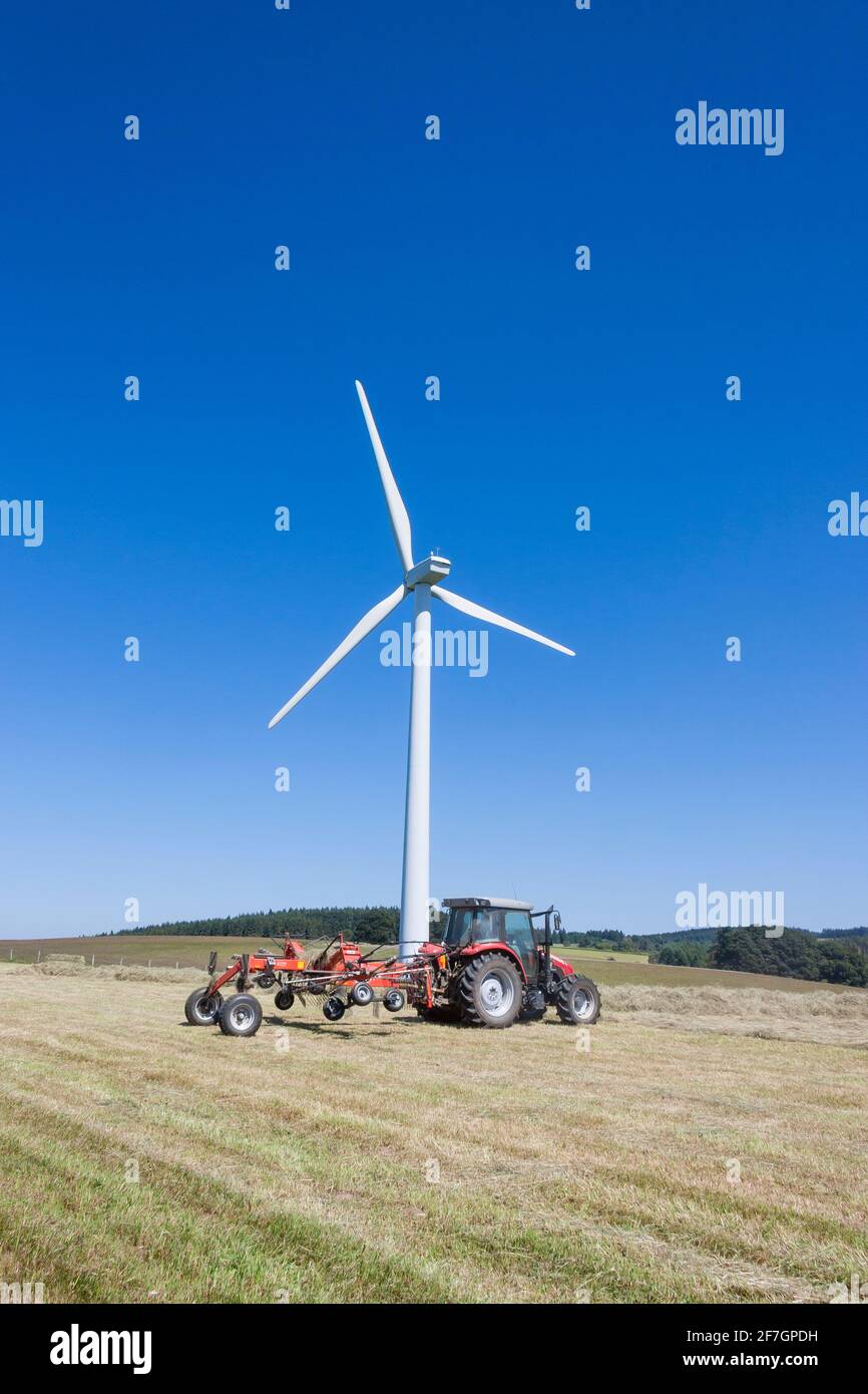 Windturbine auf Ackerland mit Landwirt Ernte Heu. Koexistenz von Landwirtschaft und erneuerbarer Energie aus der Umwandlung von kinetischer Windenergie in Elektr Stockfoto