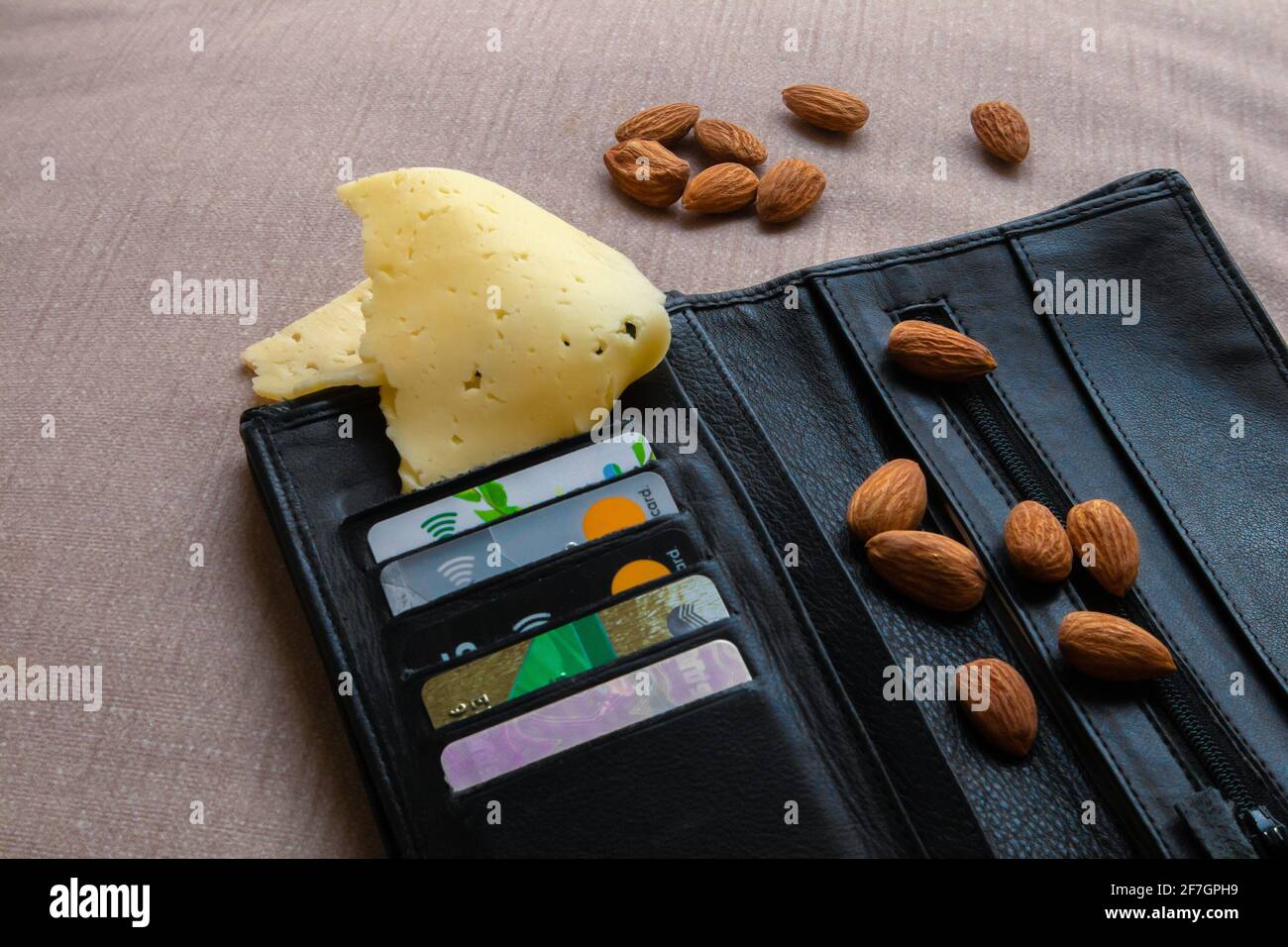 Foto-Witz, schwarze Ledertasche mit Kreditkarten, Mandel und Stück Käse, absurdes Foto Stockfoto