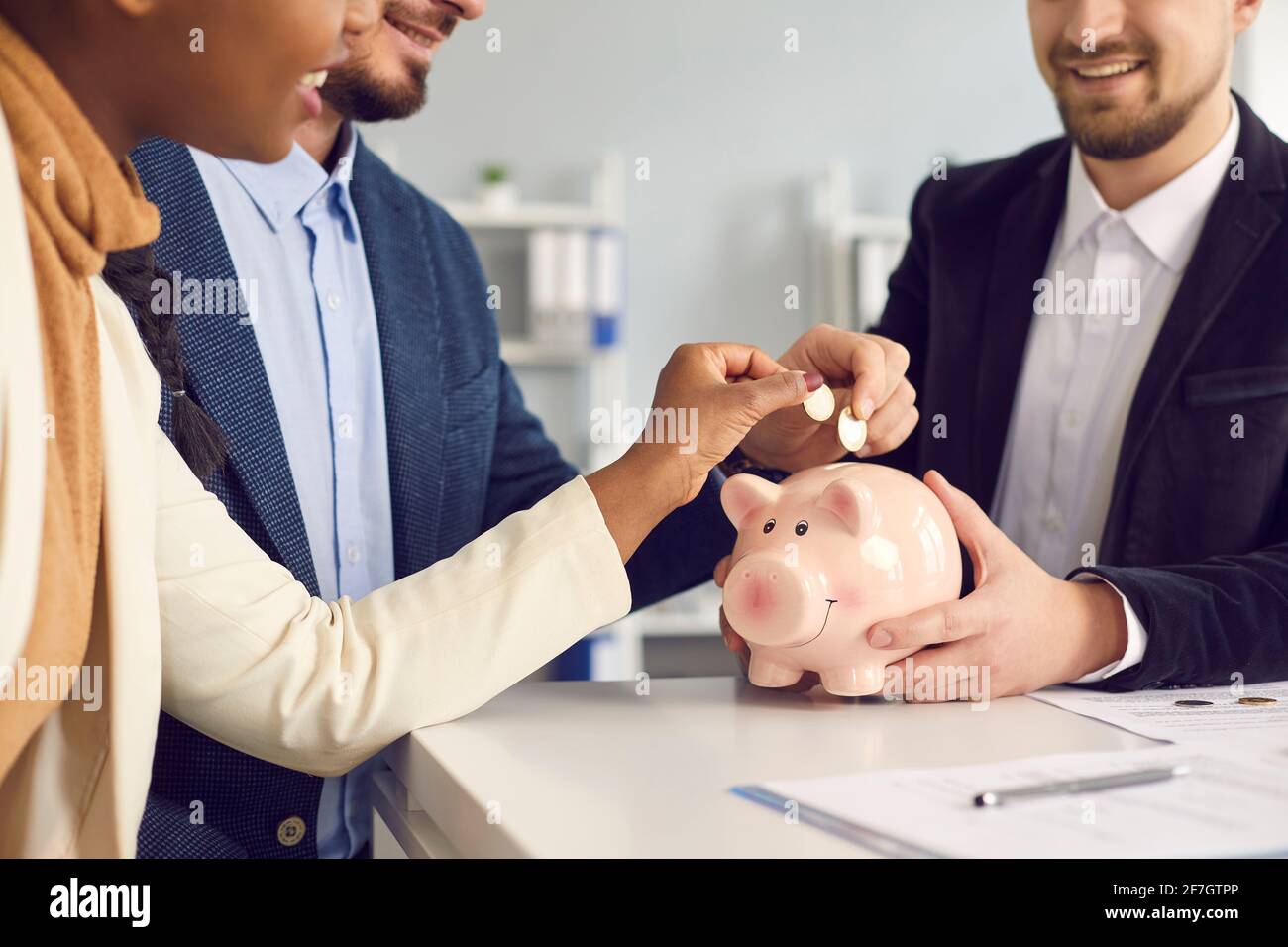 Das junge Paar steckte Geld in ein Sparschwein, das am Schreibtisch saß Mit Makler oder Finanzberater Stockfoto