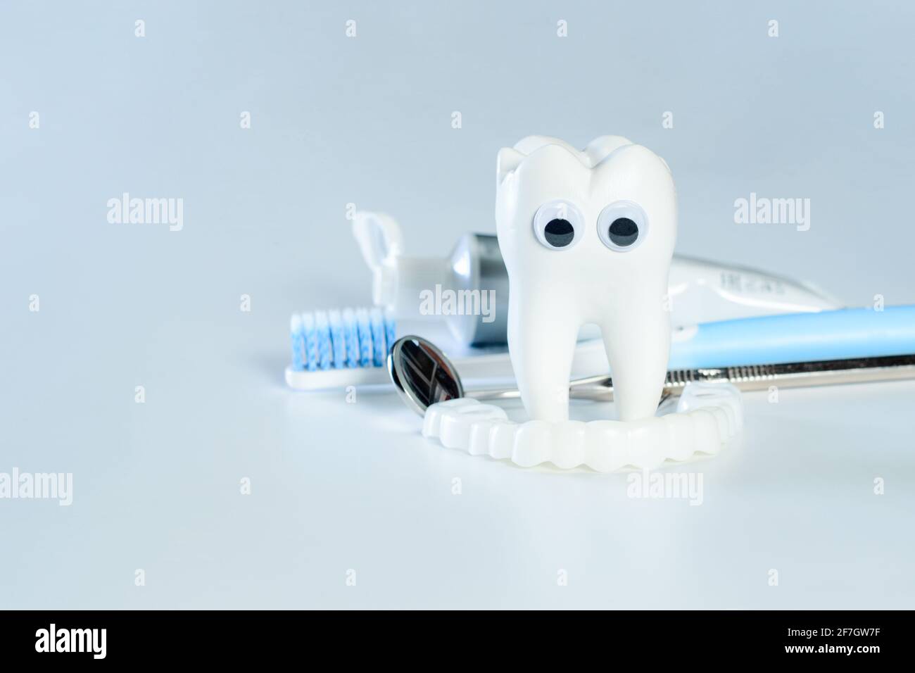 Weißer großer gesunder Zahn mit guten Augen schaut auf falsche Zähne. Daneben gibt es verschiedene Werkzeuge für die Zahnpflege. Stockfoto