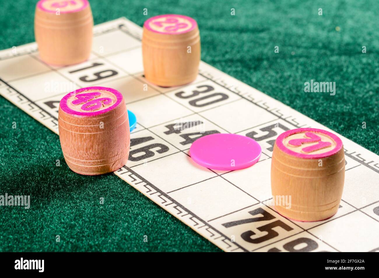 Lotto, ein klassisches Familien-Brettspiel. Drei Holzfässer mit Zahlen, roten und blauen Chips und Karte auf grüner Samtfläche während des Spiels. Vintage-Ga Stockfoto