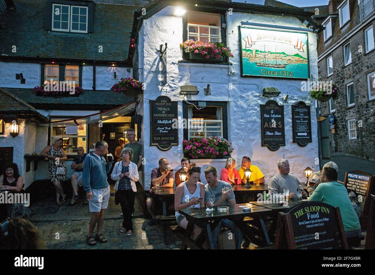 Menschen, die vor dem Pub Sloop Inn in St. Ive's Harbour, Cornwall, Großbritannien, sitzen. Stockfoto