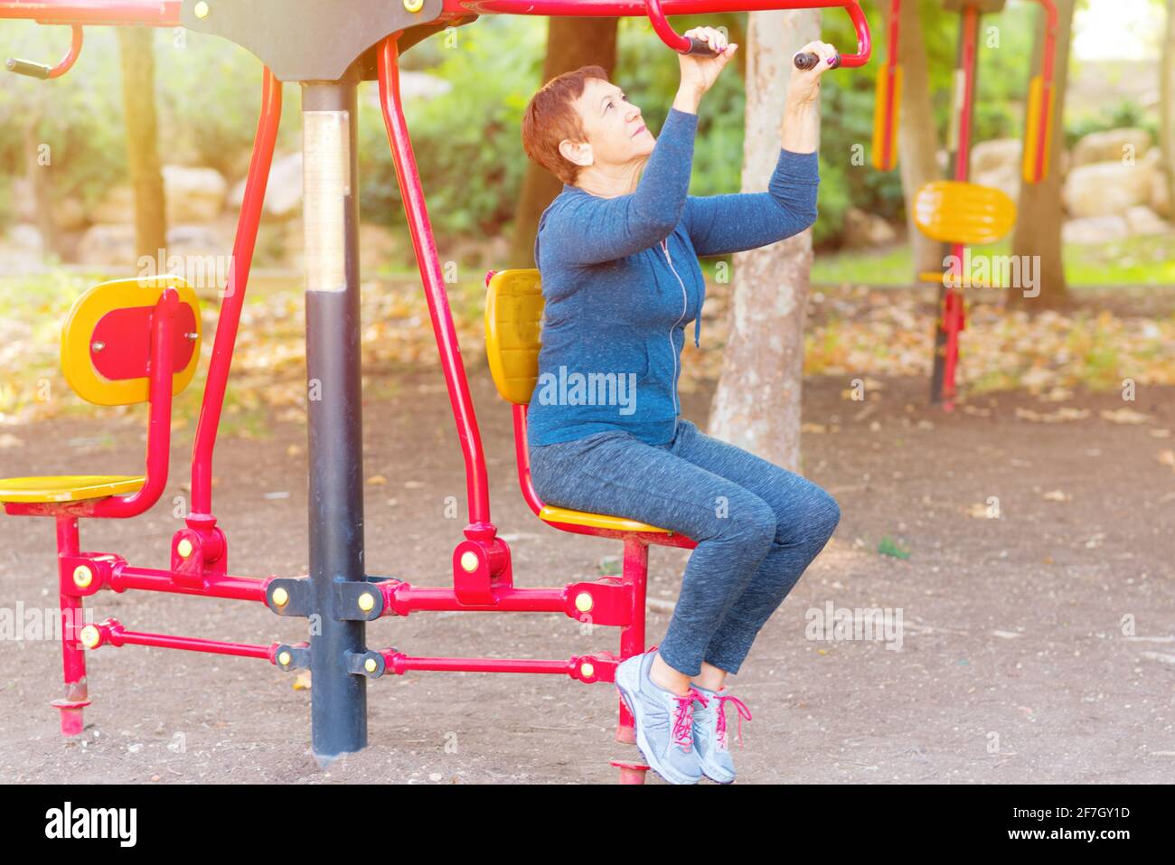 Ältere Frau im Alter von 60-70 Jahren, die an den öffentlichen Sportgeräten im Fitnessstudio im Freien trainiert.EINE sportlich aktive ältere Frau, die an sonnigen Tagen in einem Park Sport macht. Stockfoto