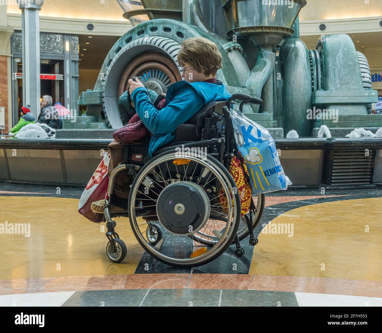 Niagara, Ontario, Kanada, März 2018 - Junge kaukasische Frau mit Behinderung beim Schreiben oder Lesen im Rollstuhl auf ihrem Handy Stockfoto