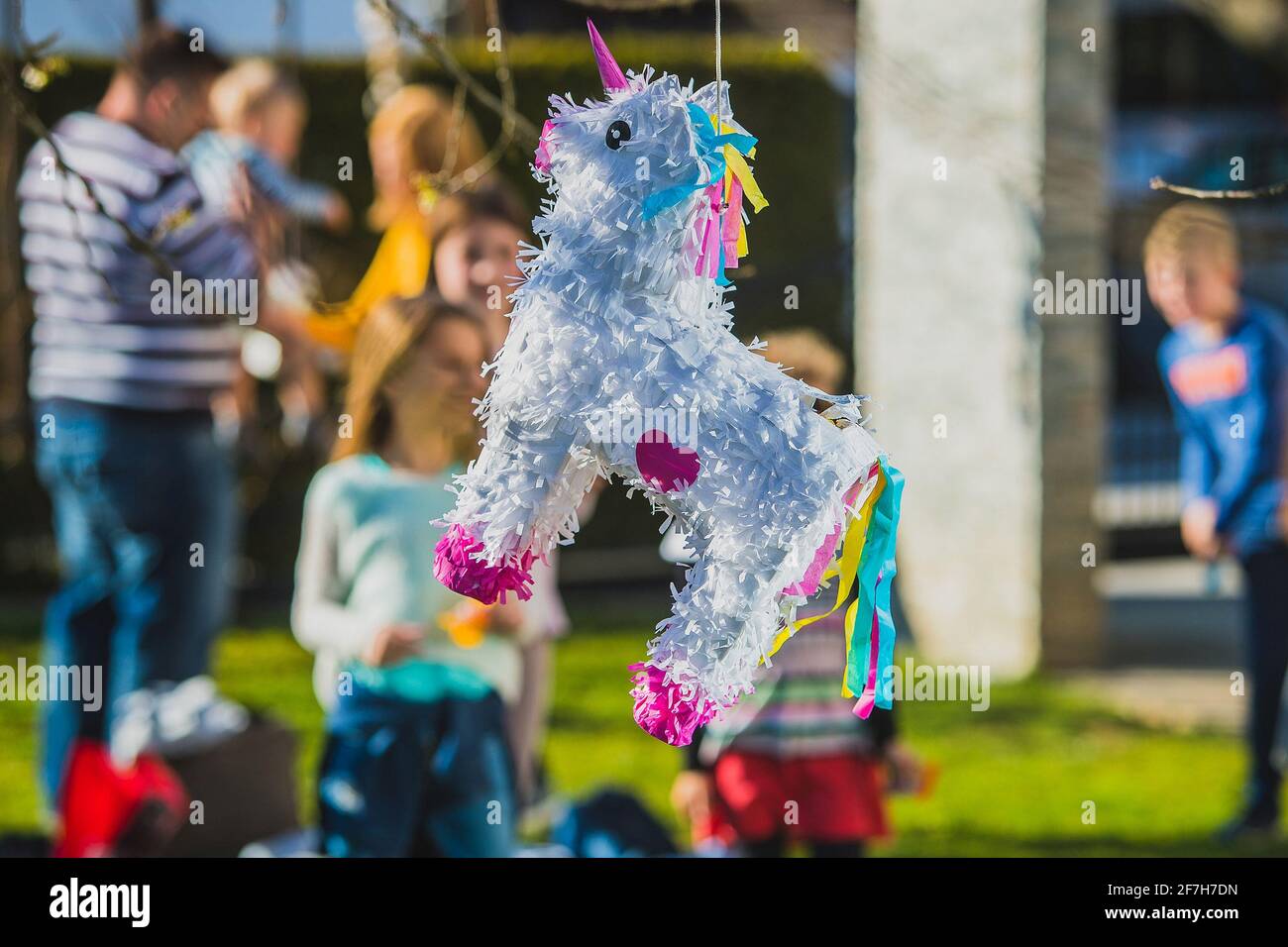 Weiße, auf dem Baum hängende, Esel-förmige Pinata mit Kindern, die darauf warten, sie im Hintergrund zu treffen. Festliche Aktivität während eines Geburtstages Stockfoto