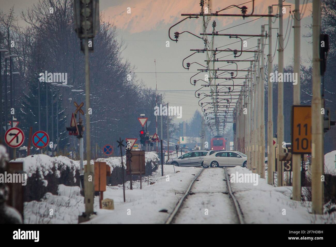 Der rote Zug kommt auf den Bahnübergang zu, während noch Autos über den Bahnübergang fahren. Konzept der Gefahrensituation bei Bahnübergängen. Stockfoto
