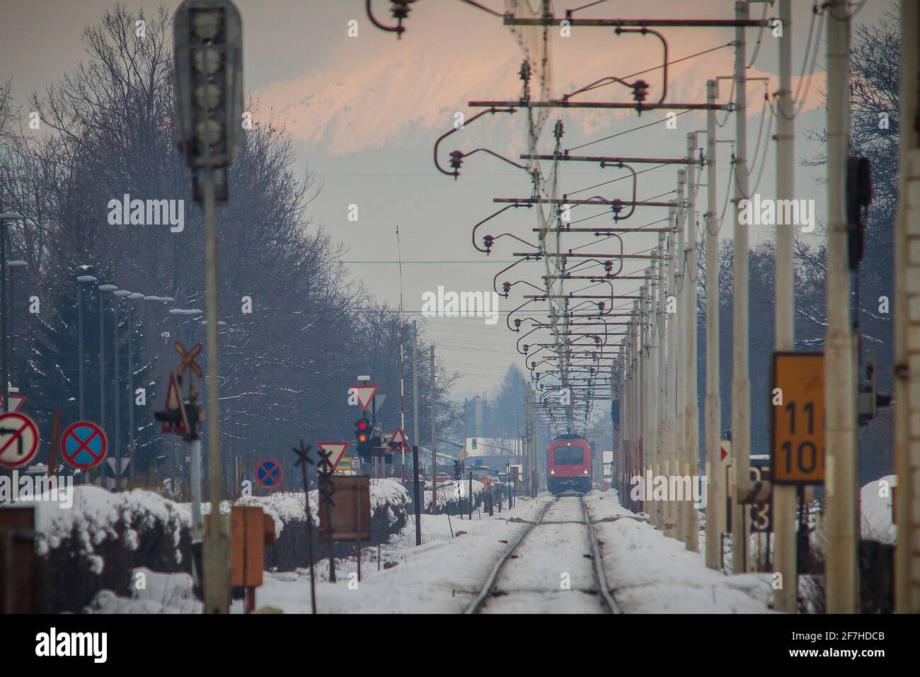Der rote Zug kommt zum Bahnübergang, die Autos fahren gerade nicht mehr über den Bahnübergang. Konzept der Gefahrensituation bei Bahnübergängen. Stockfoto