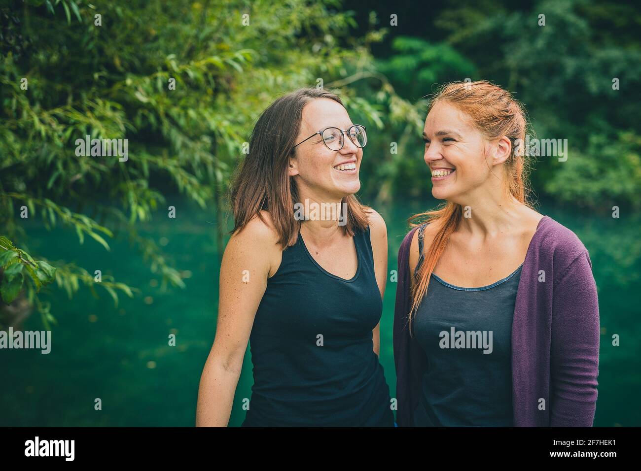 Porträt von zwei jungen Frauen, Brünette und einem Rotschopf mit schwarzen Panzerplatten, die Spaß haben und sich an einem nebligen Tag an einem Fluss umsehen. Wasser und Bäume Stockfoto