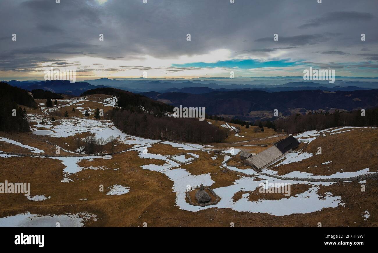 Drohne Bergpanorama der Holzkirche mit Zaun auf einer Bergplatte der Biba planina in den slowenischen Alpen umgeben. Früher Frühling mit Flecken von sn Stockfoto