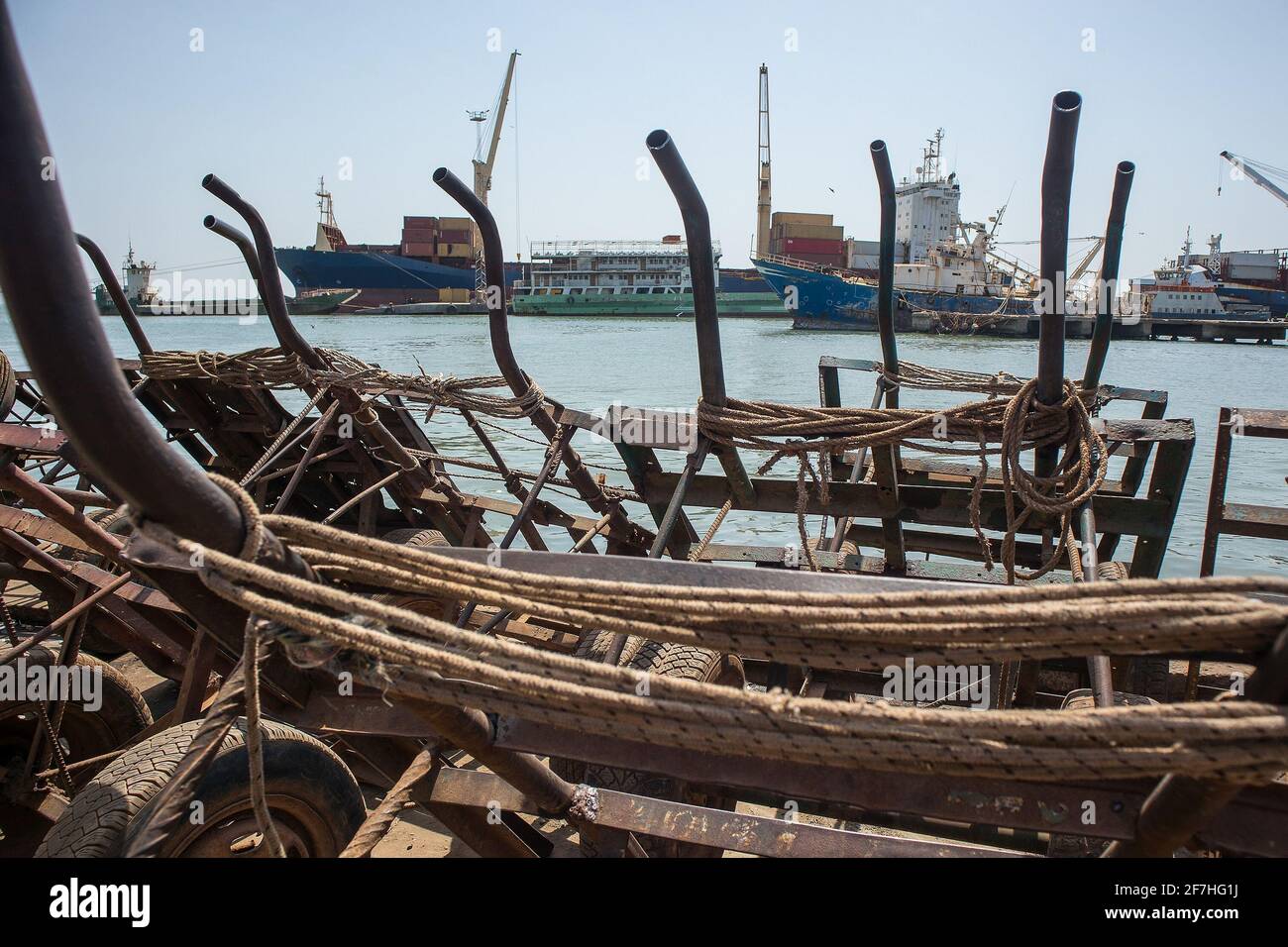 Eine Sammlung von primitiven Metallwagen oder Karren mit Autorädern in einem Fährhafen für den Transport von Waren. Schiffe vertäuten im Hintergrund in einem Hafen. Ha Stockfoto