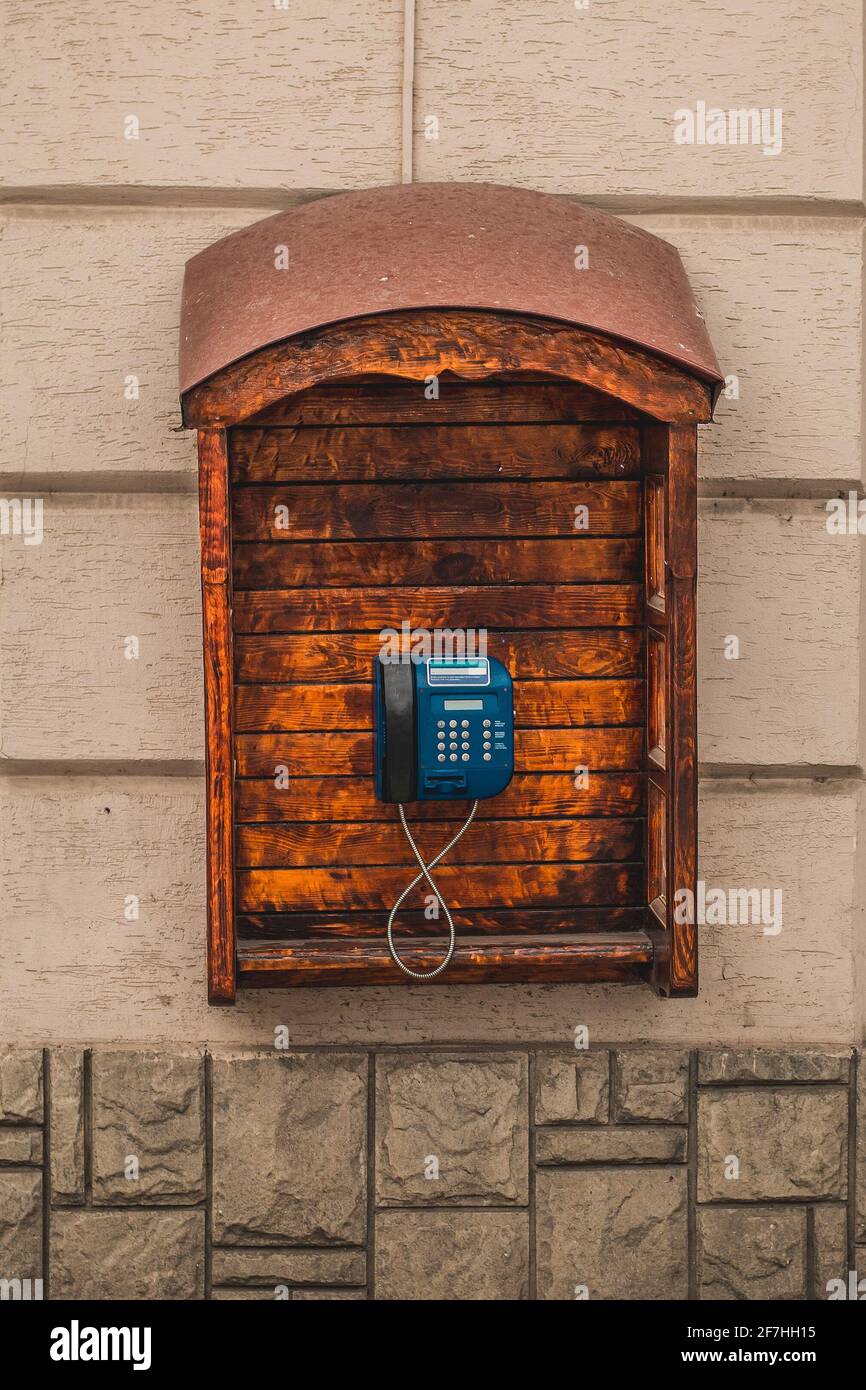 Typisches öffentliches Telefon in Lviv, Ukraine, in einer hölzernen Kabine oder Box. Braunes Holz, das ein blaues öffentliches Telefon umgibt und schützt. Stockfoto