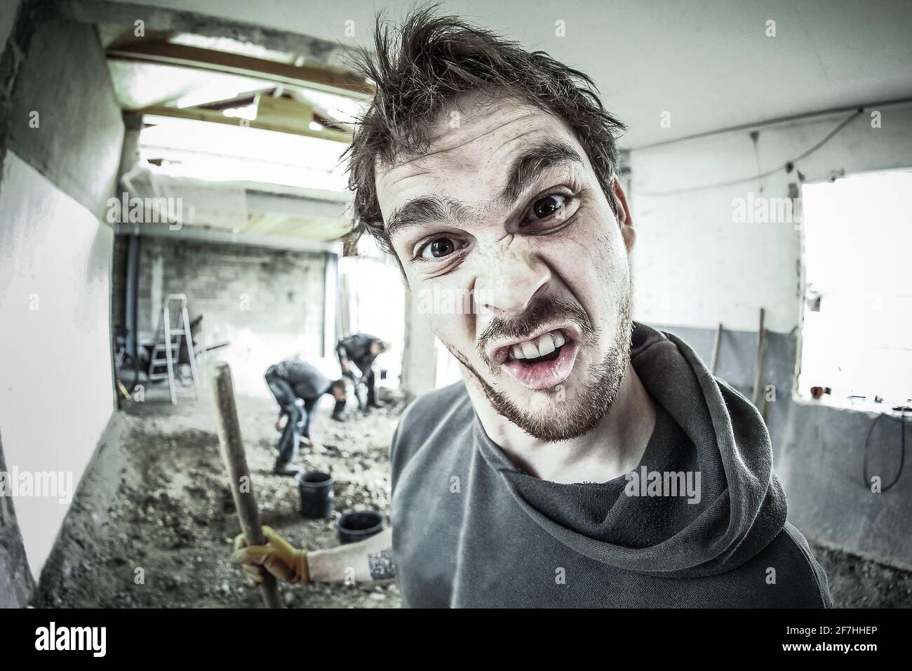 Ein Arbeiter, der ein dummes Gesicht beim Renovieren eines Hauses macht. Andere Arbeiter im Hintergrund. Fisheye-Ansicht. Stockfoto