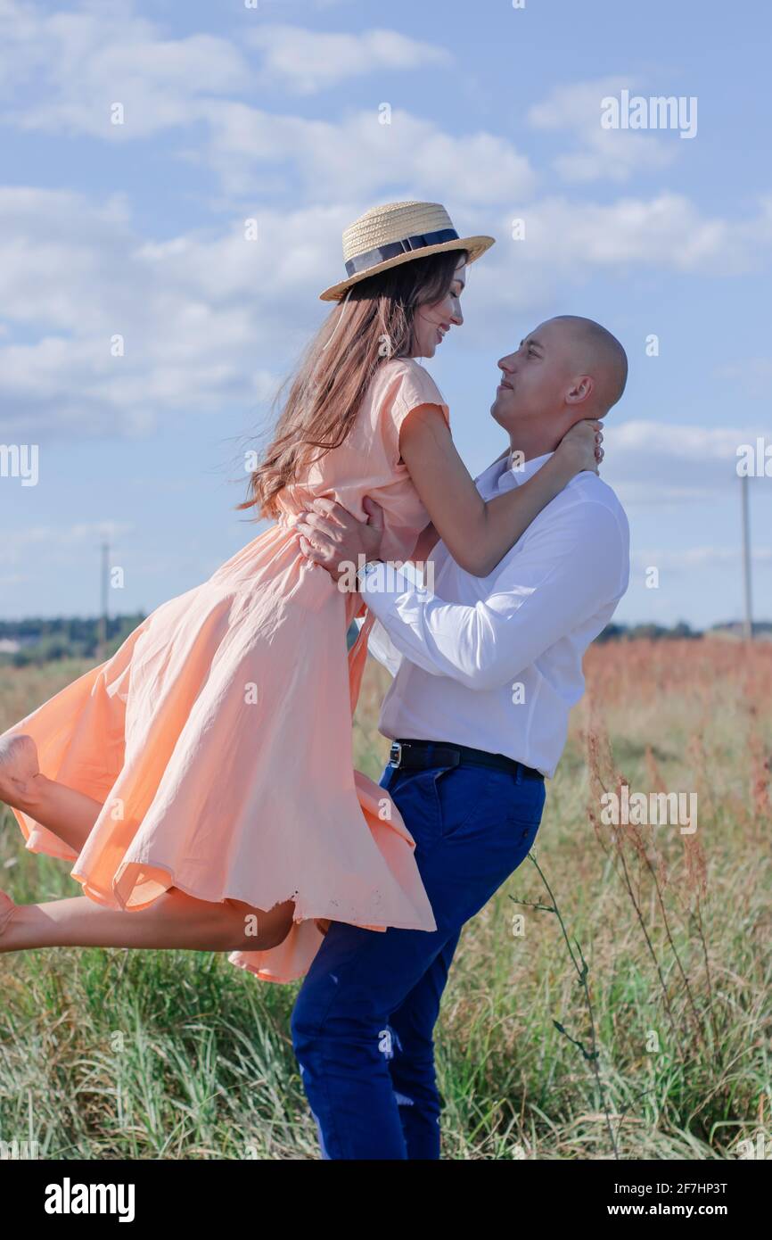 Glückliches Paar tanzt auf dem Feld. Brunette in cremefarbenem Kleid und kahler Mann in weißem Hemd und blauer Hose. Ehemann und Ehefrau auf einem romantischen Date. Liebesgeschichte Stockfoto