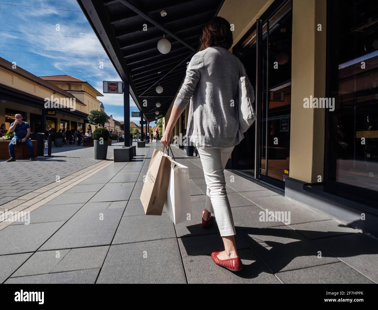 Rückansicht einer alleinstehenden Frau, die mit auf die Gasse geht Mehrere  Geschäfte im Roppenheim The Style Outlet mit Papier Taschen mit Aigle und  anderen Marken Stockfotografie - Alamy