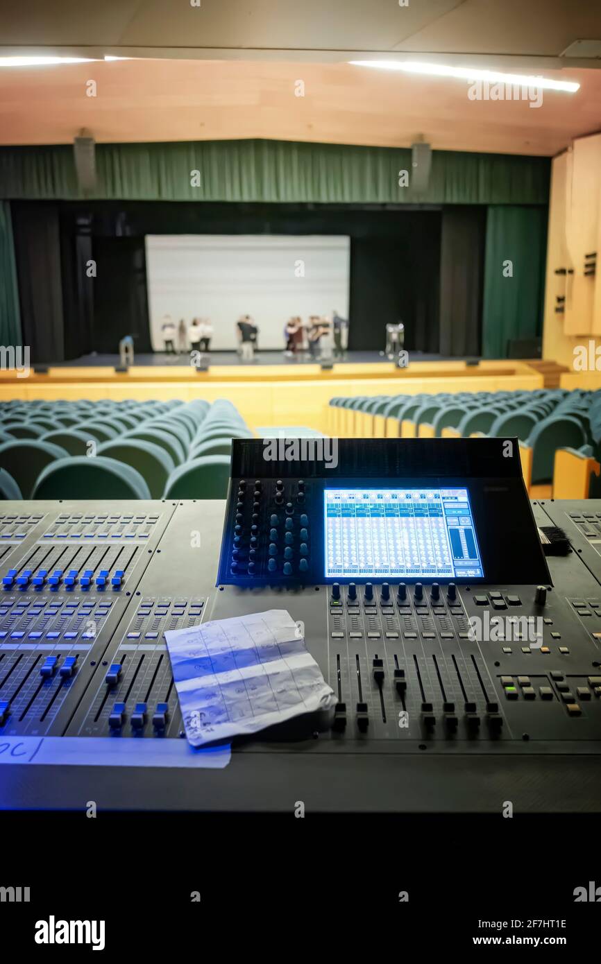 Theater-Sound- und Lichtsteuerungstisch, vom Bedienfeld aus gesehen, mit der Bühne im Hintergrund, mit Künstlern, die außerhalb des Fokus Proben, vertikal Stockfoto