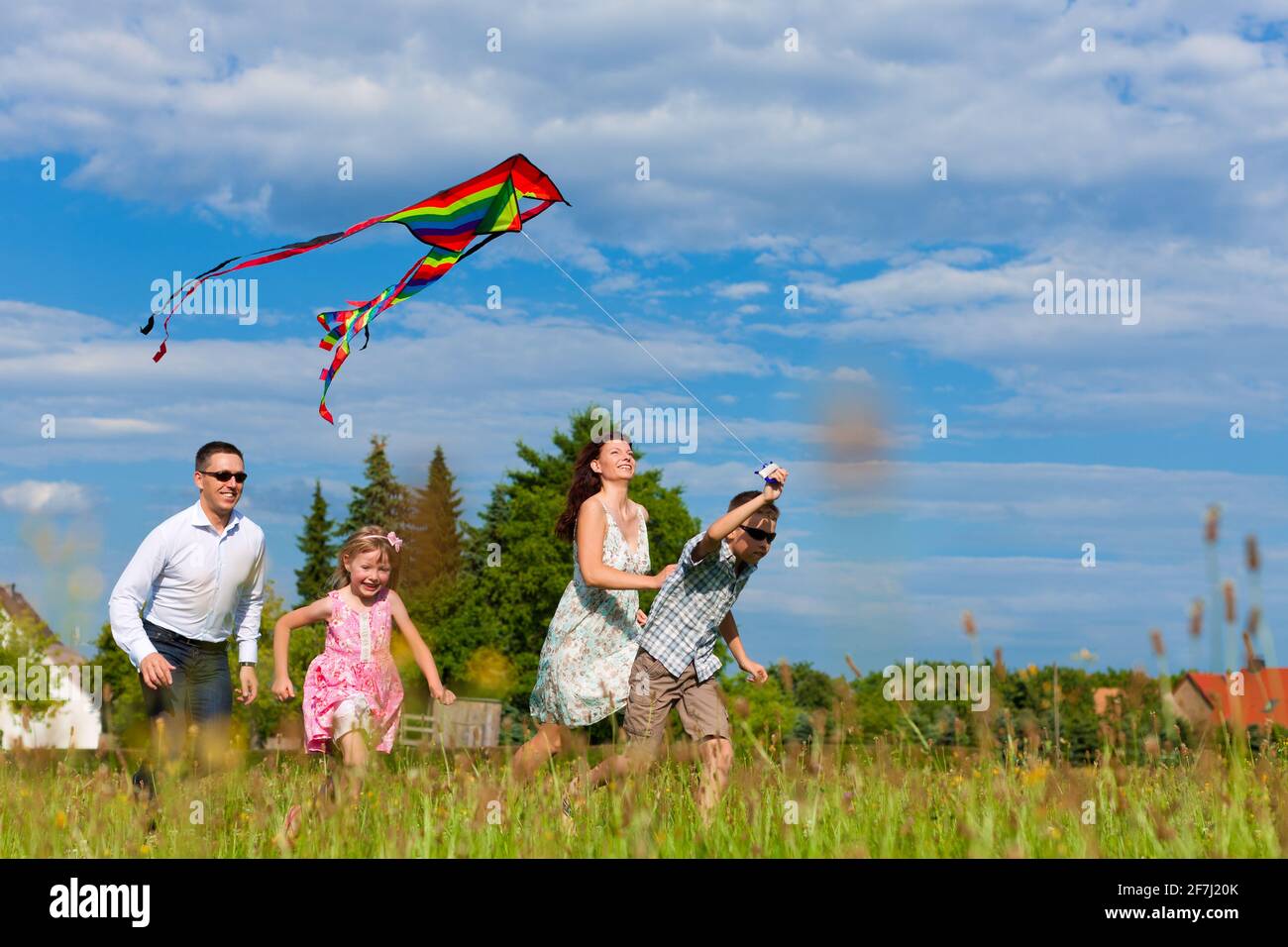 Glückliche Familie - Mutter, Vater, Kinder - die im Sommer über eine grüne Wiese laufen; sie fliegen einen Drachen Stockfoto