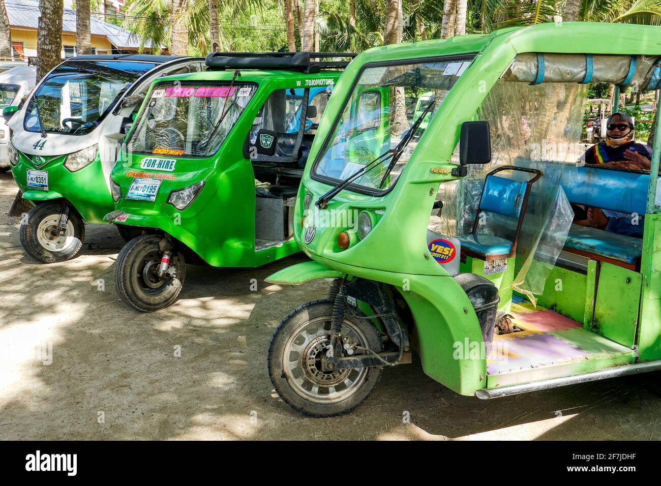 Drei grüne elektrische Trikes parken in der Nähe des Hafens von Cagban auf der Insel Boracay auf den Philippinen und warten auf Passagiere. Ein Fahrer im Trike sichtbar. Stockfoto
