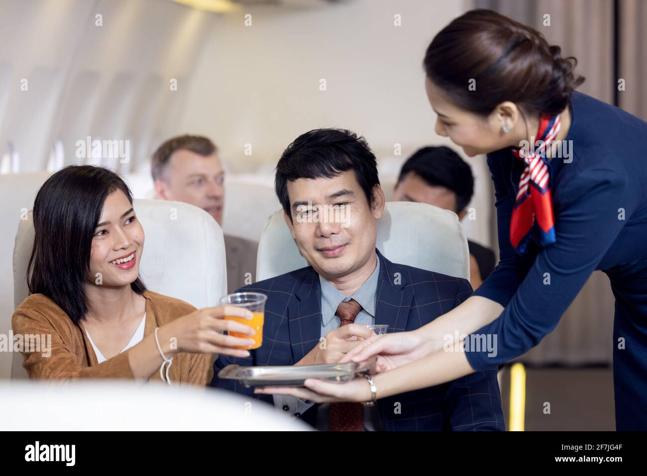 Der Passagier wird von einer Flugbegleiterin im Flugzeug mit Orangensaft serviert, die Flugbegleiter sind an Bord Stockfoto