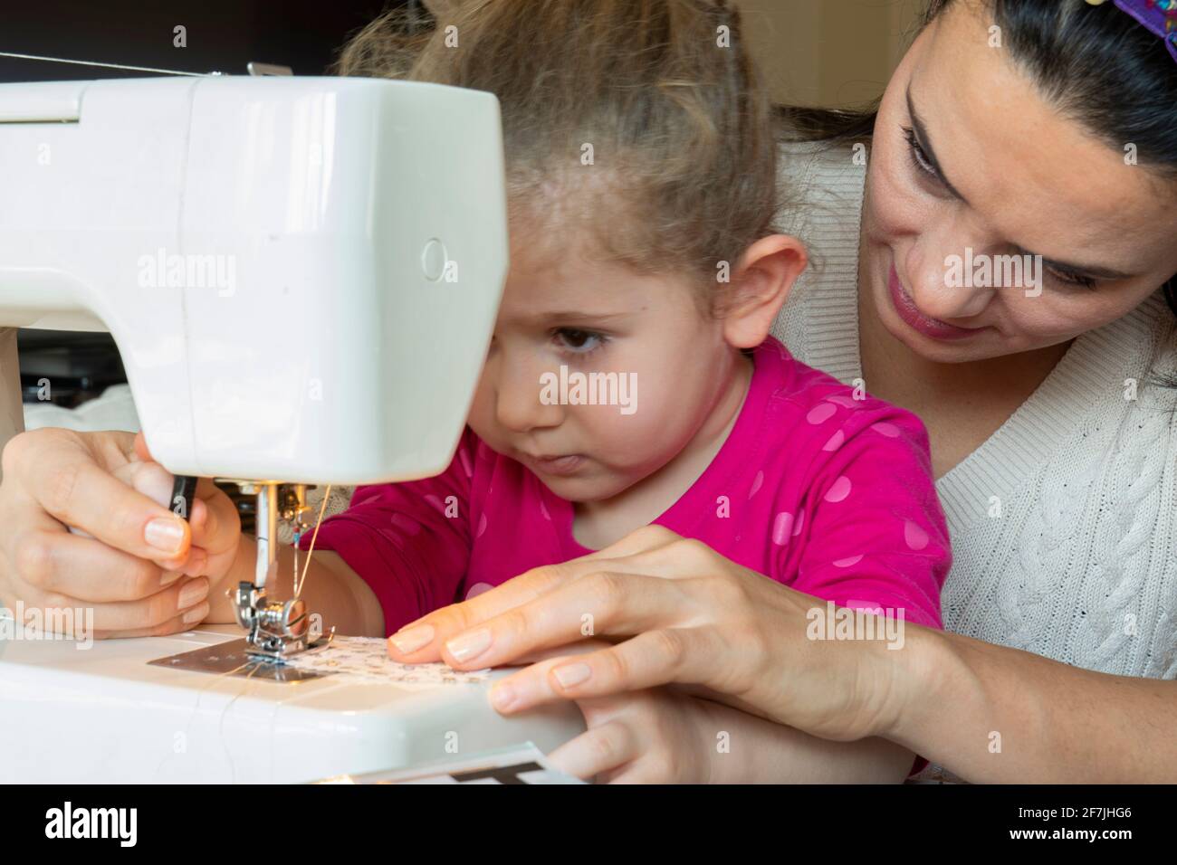 Kleines Mädchen lernt von ihrer Mutter, eine Nähmaschine zu verwenden Stockfoto