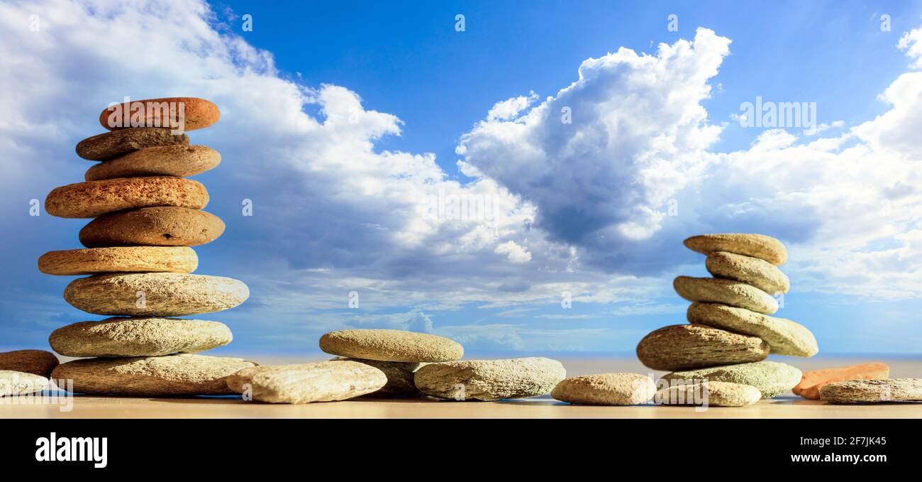 Zen-Steine gestapelt auf blau bewölktem Himmel, Meerwasser, Strand im Hintergrund. Kieselsteinpyramide, Yoga, Meditation und Gleichgewicht, Harmonie, Gleichgewicht, Alternativ Stockfoto