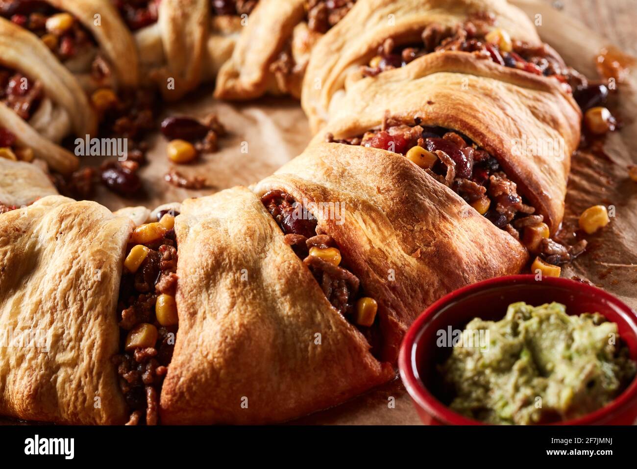 Nahaufnahme von leckeren knusprig gebackenen mexikanischen Enchilada Ring gefüllt mit Fleisch und Bohnen mit Mais serviert mit Guacamole-Sauce Stockfoto
