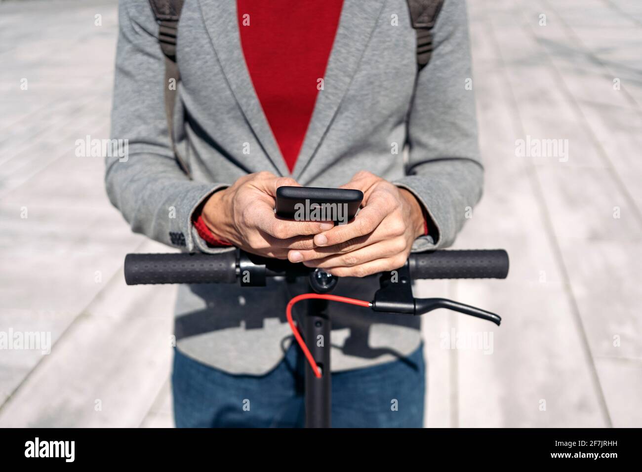 Stock Foto von einem Geschäftsmann in Jacke mit Rucksack Stehen auf Elektroroller und mit Smartphone Stockfoto