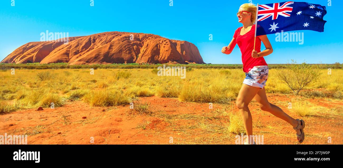 Fröhliche Lifestyle-Frau, die mit der australischen Flagge im australischen Outback Red Centre läuft. Tourismus im Northern Territory, Zentralaustralien. Uluru Ayers Stockfoto