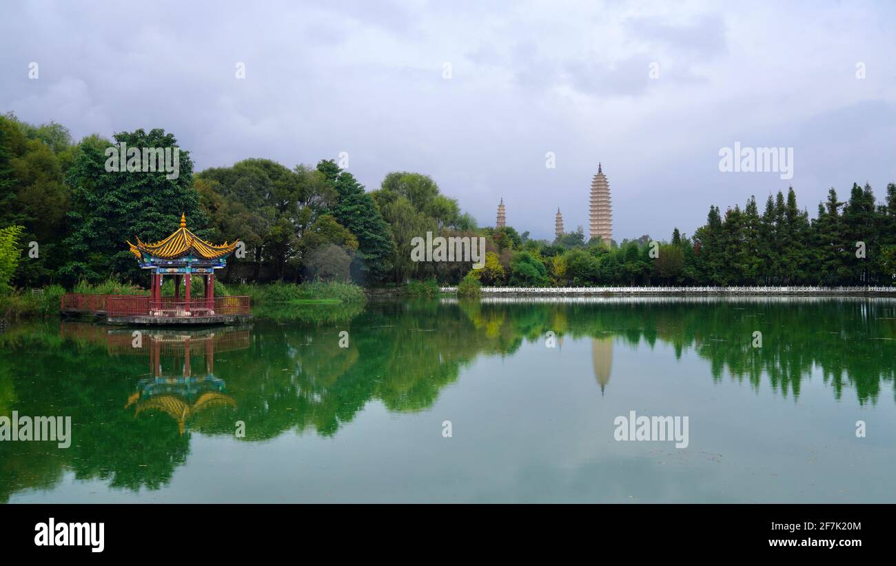 Drei Pagoden des Chongsheng-Tempels in Dali, Yunnan, mit ihrer Reflexion über stilles Wasser des Teiches, umgeben von grünen Bäumen. Stockfoto