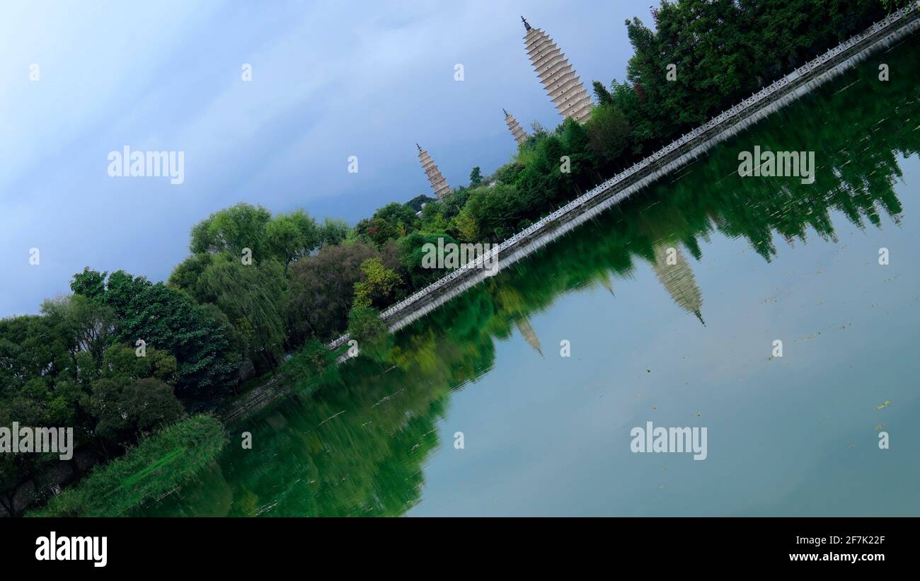 Drei Pagoden des Chongsheng-Tempels in Dali, Yunnan, mit ihrer Reflexion über stilles Wasser des Teiches, umgeben von grünen Bäumen. Stockfoto