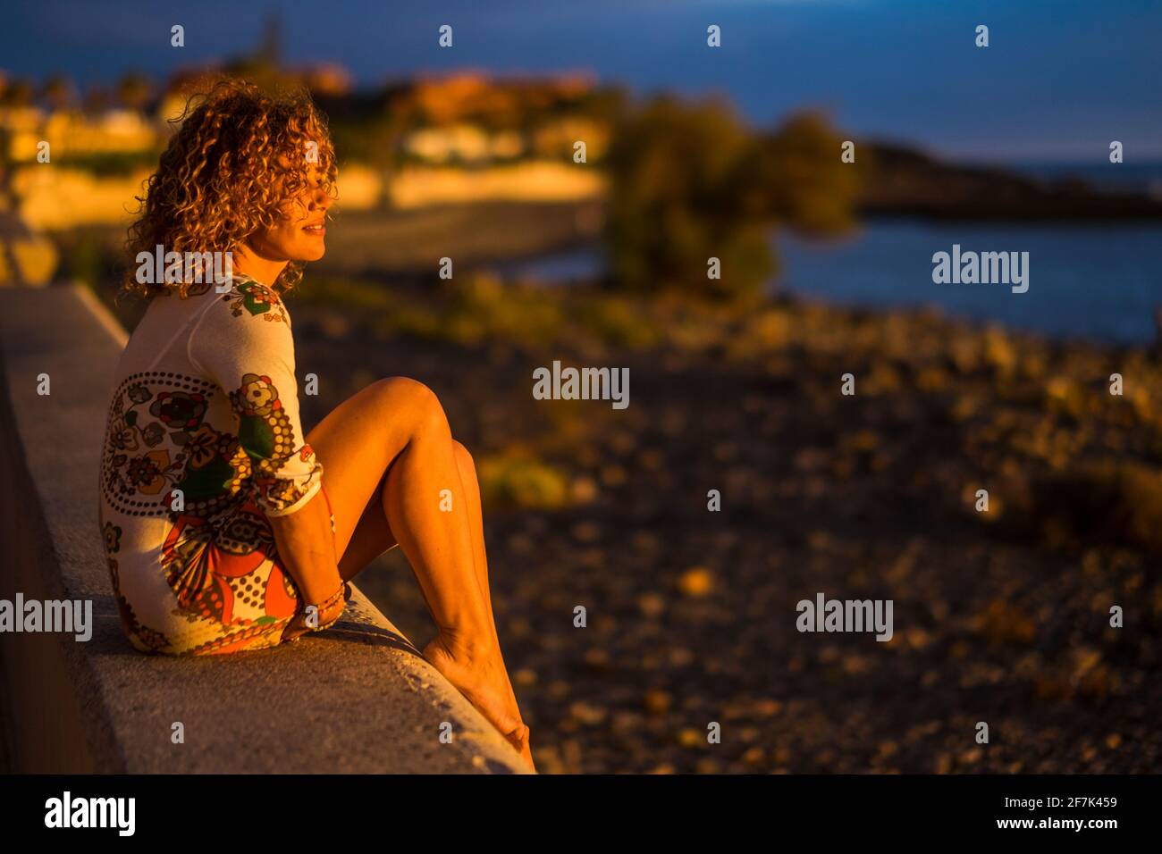 Eine Frau setzt sich draußen hin und genießt das Sonnenuntergang-Licht Vor ihr - Strand und Meer im Hintergrund - Tourismus und Sommerurlaub Reisen Stockfoto