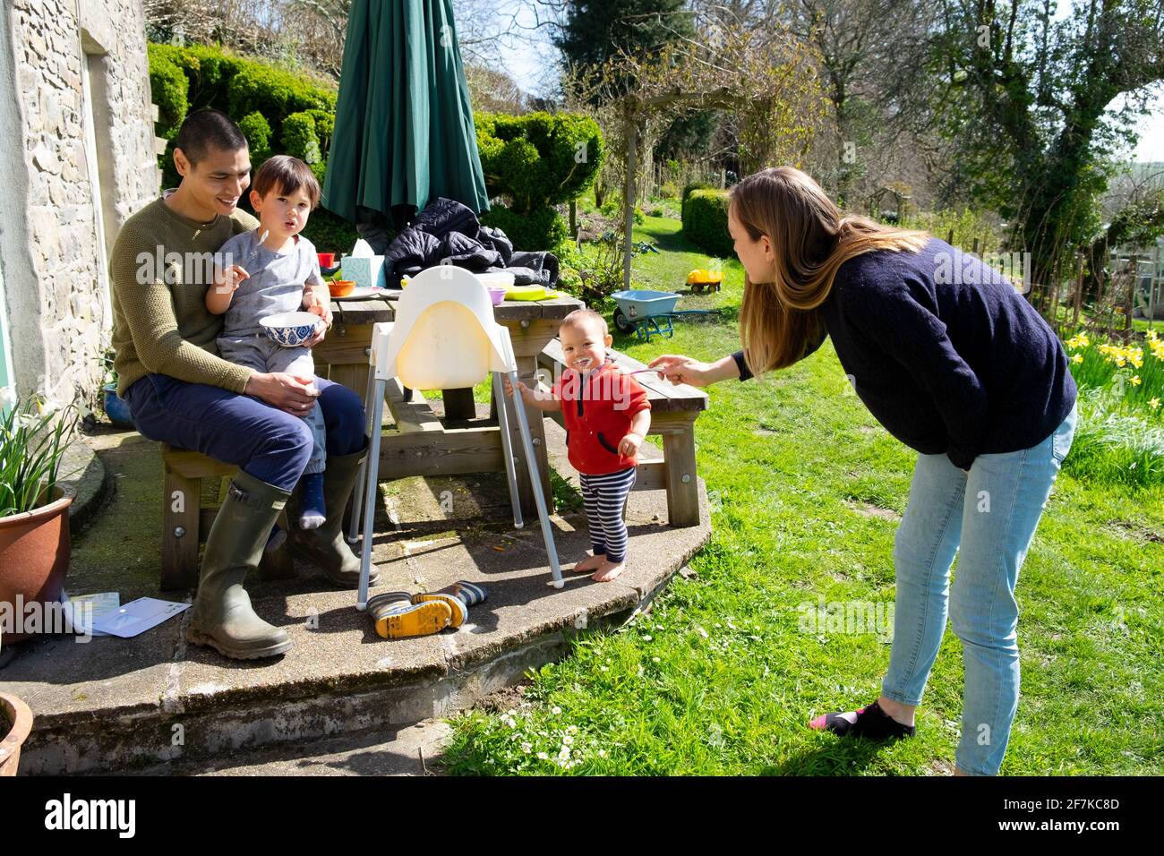 Eltern Mutter Vater junge Familie sitzt mit Kindern außerhalb des Hauses Am sonnigen Osterwochenende in einem Garten in West Wales UK KATHY DEWITT Stockfoto