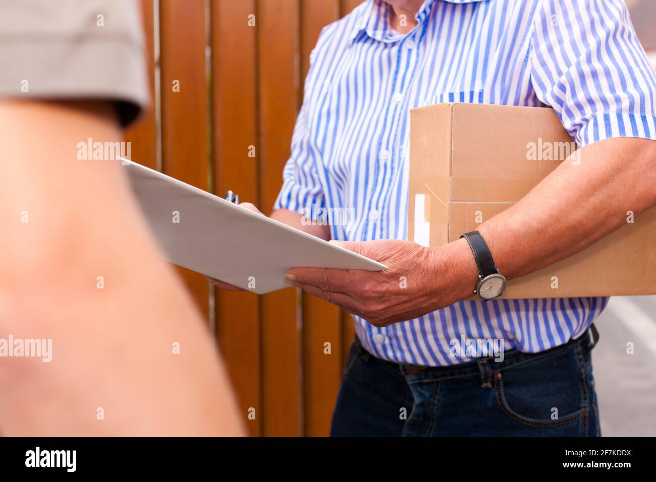 Postdienst - Lieferung eines Pakets; der Postbote gibt dem Kunden das Paket vor seinem Haus; der Kunde erhält die Lieferung Stockfoto