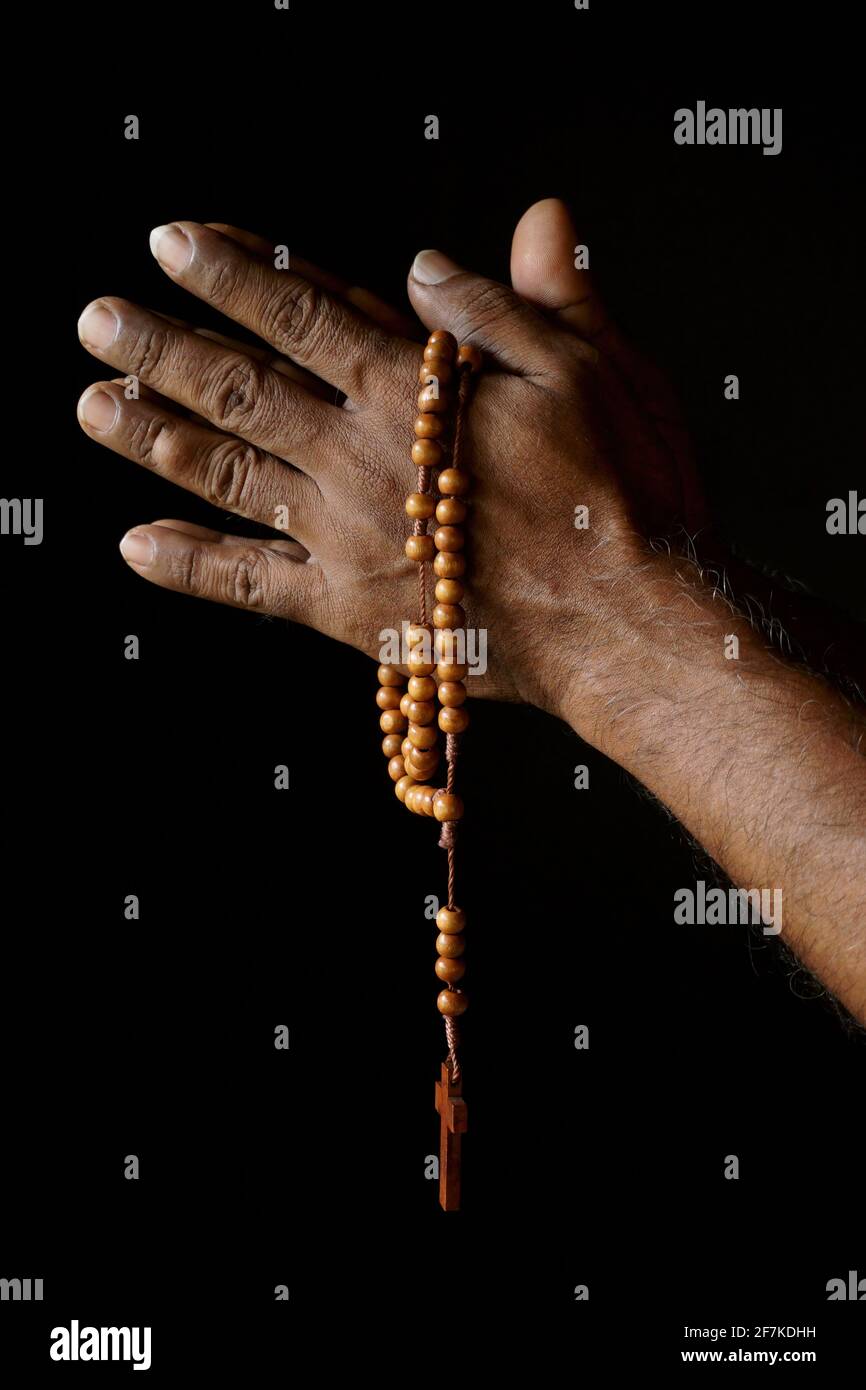 Betende Hand eines alten indischen katholischen Mannes mit hölzernen Rosenkranz isoliert auf einem schlichten schwarzen Hintergrund. Stockfoto