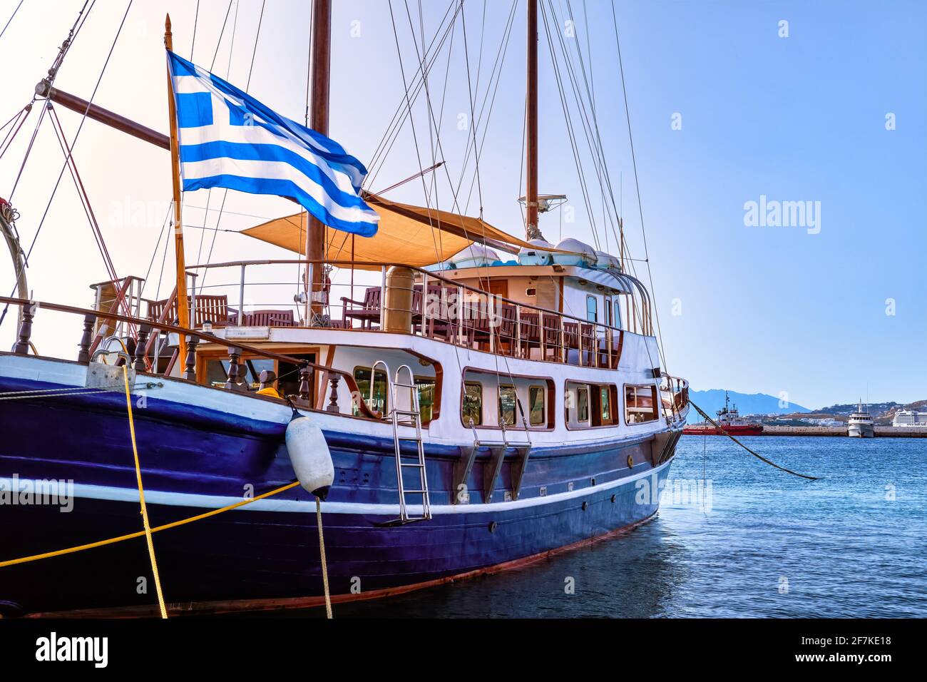 Segelboot unter griechischer Flagge, der an der Anlegestelle der typisch griechischen Insel festgemacht ist. Schoner. Sommertag Sonne, Urlaub und Abenteuer. Mykonos, Griechenland. Stockfoto