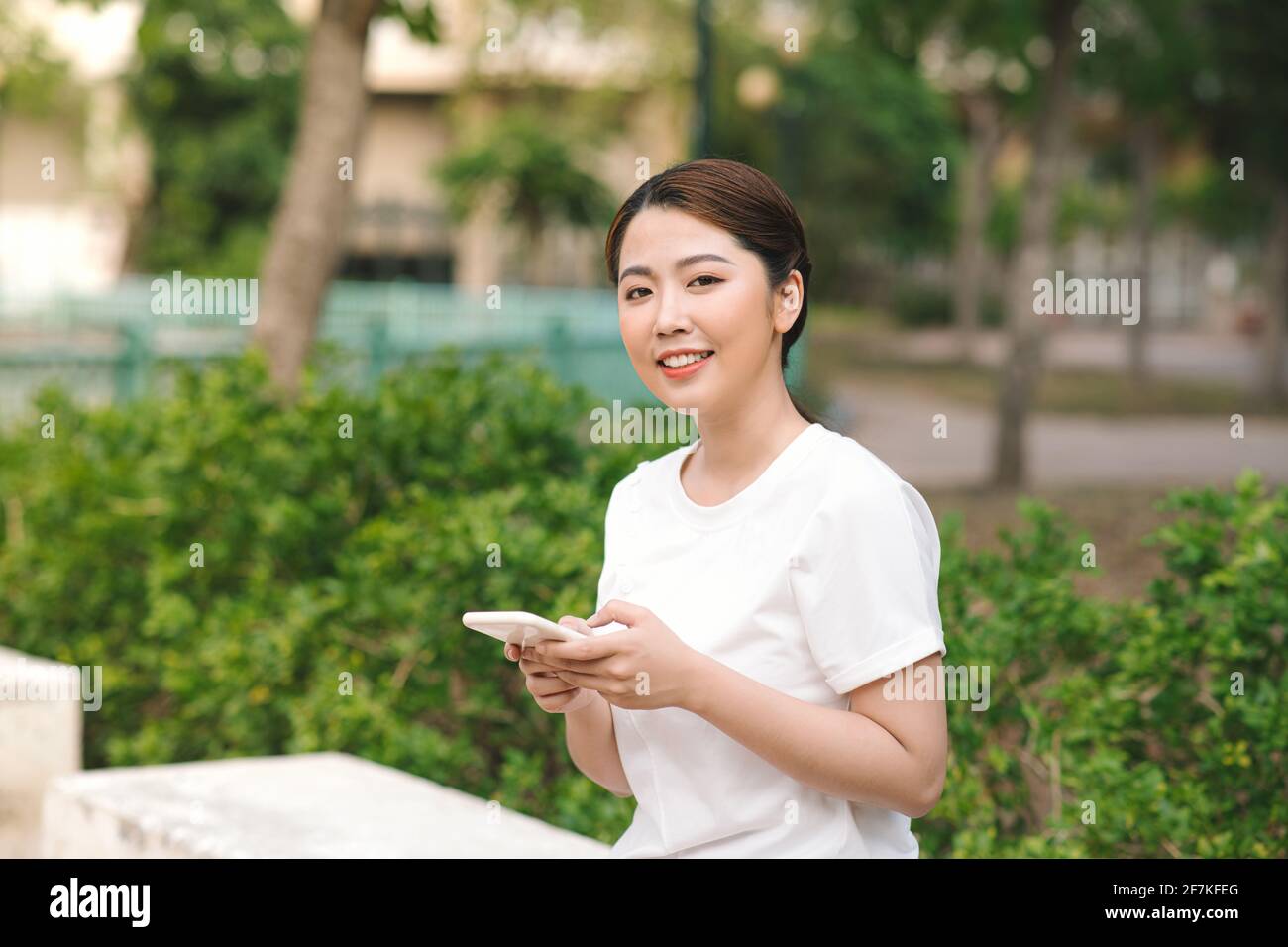 Foto einer glücklich lächelnden jungen Frau im grünen Naturpark im Freien mit dem Mobiltelefon. Stockfoto