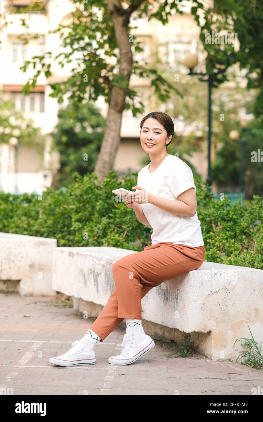 Foto einer glücklich lächelnden jungen Frau im grünen Naturpark im Freien mit dem Mobiltelefon. Stockfoto