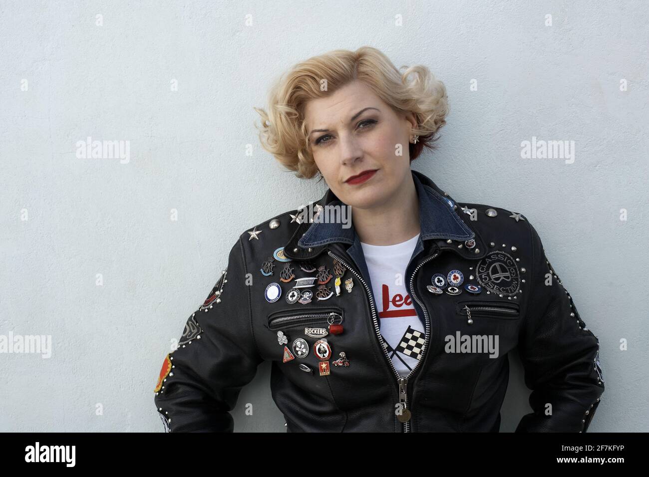 Schöne blonde weibliche Biker, Cafe Racer trägt eine Lederjacke mit Nieten, Patches und Abzeichen bedeckt. Stockfoto