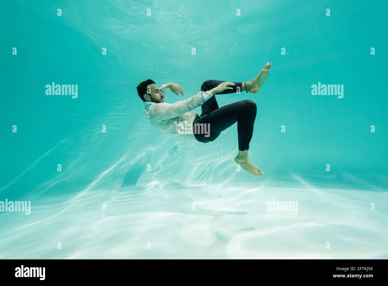 Arabischer Geschäftsmann in Hosen und Hemden, der im Pool unter Wasser schwimmend ist Stockfoto