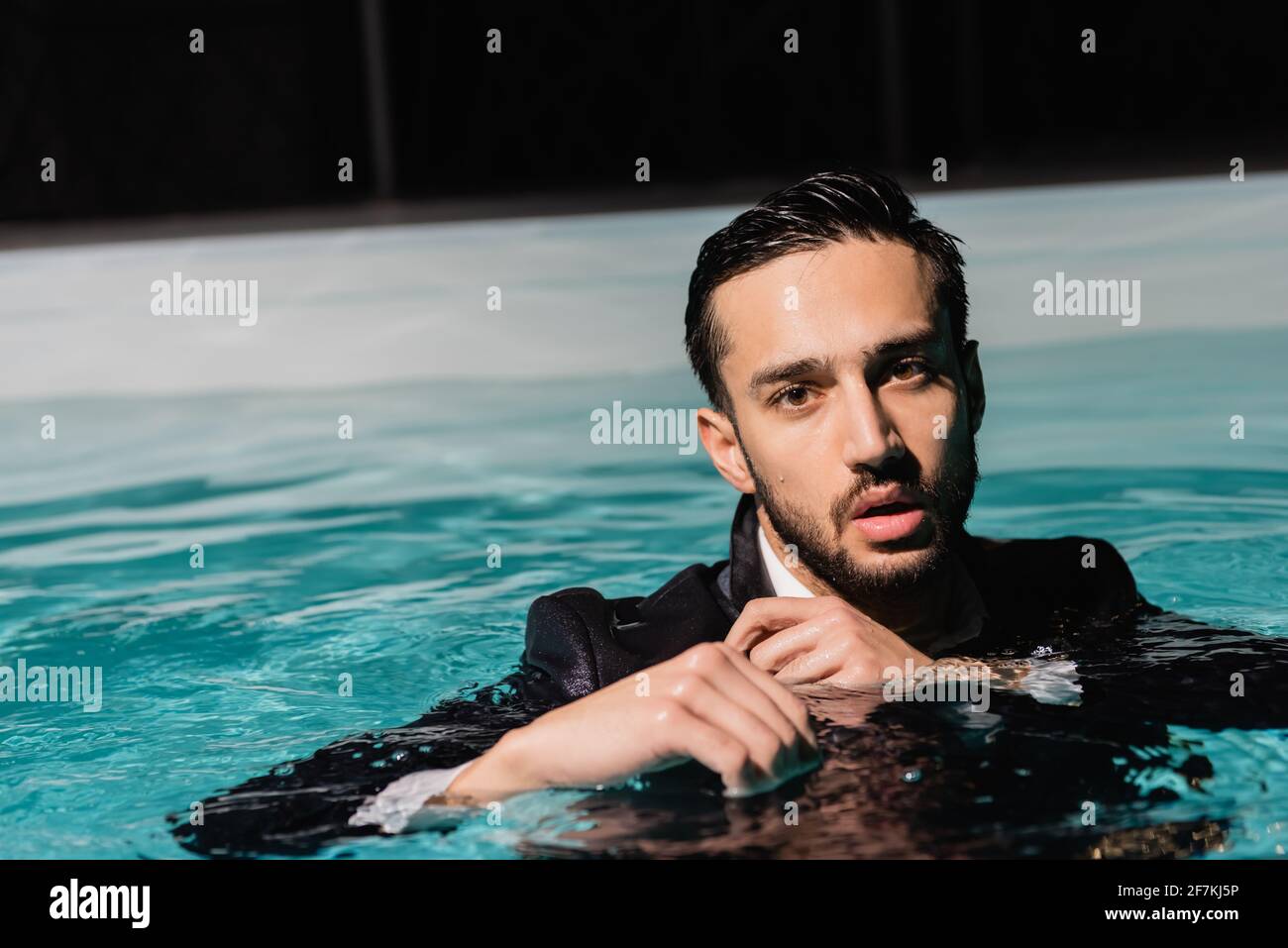 Ein arabischer Geschäftsmann im Anzug, der im Pool die Kamera anschaut Stockfoto