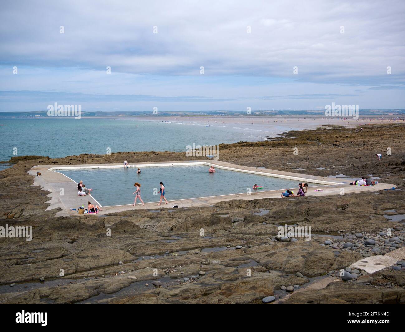 Menschen, die das Gezeitenschwimmbad Rock Pool im Küstendorf Westward Ho!, North Devon, England, genießen. Stockfoto