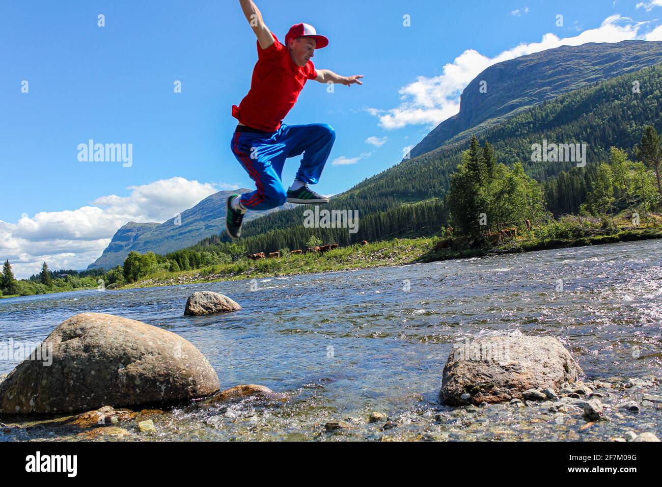 Teenager springt über einen See Hemsila mit Bergpanorama in Hemsedal Norwegen. Stockfoto