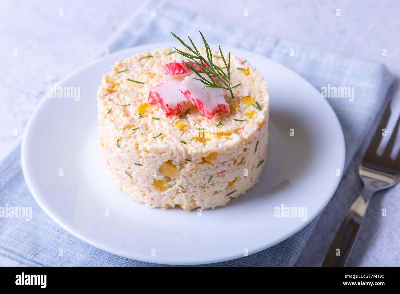 Krabbensalat mit Mais und Eiern auf einem weißen Teller. Portioniert servieren. Traditioneller russischer Salat. Nahaufnahme. Stockfoto