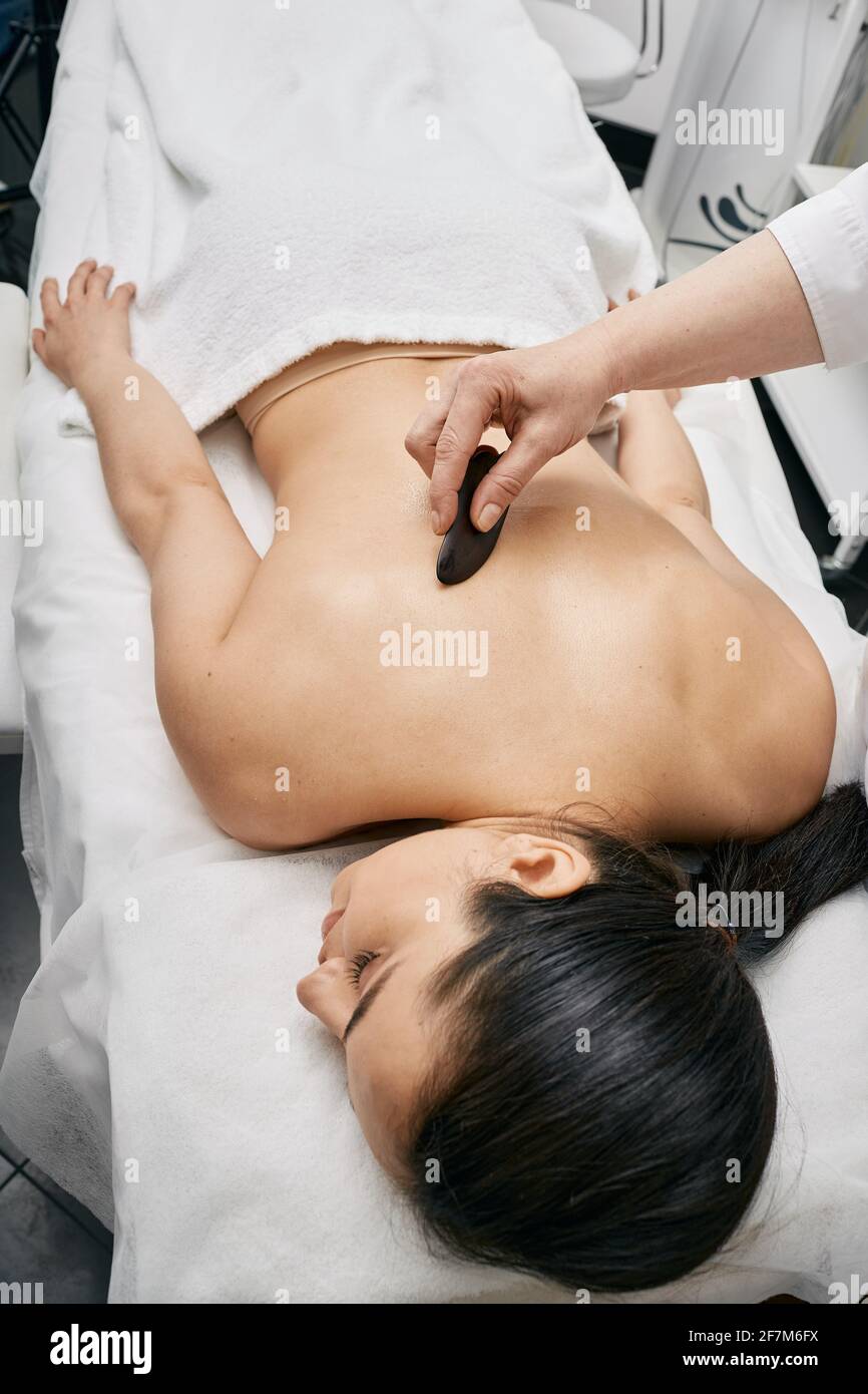 Gouache-Massage. Arzt, der eine körperliche Wirkung auf den Körper der Frau mit einem Gouache-Schaber für erhöhten Blut- und Lymphfluss macht Stockfoto