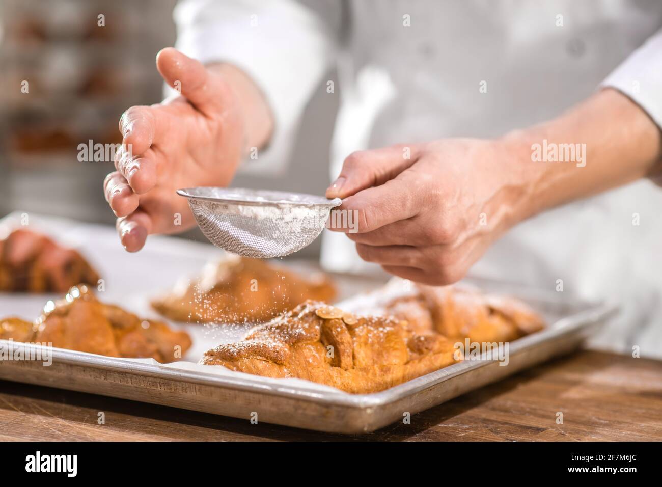 Köche reichen mit einem kleinen Sieb über das Backen Stockfoto