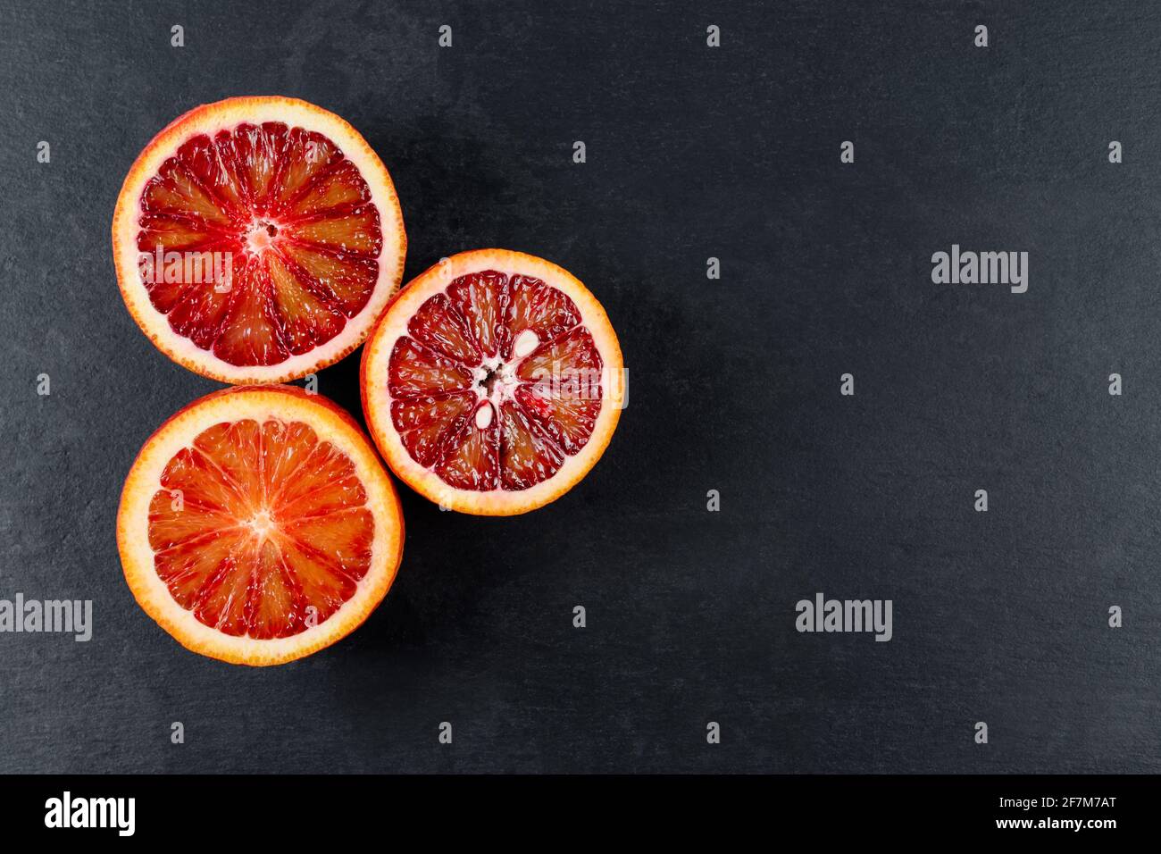 Blutige Orangen auf schwarzem Schieferbrett in zwei Hälften geschnitten. Rote sizilianische Orangenfrucht. Draufsicht. Stockfoto