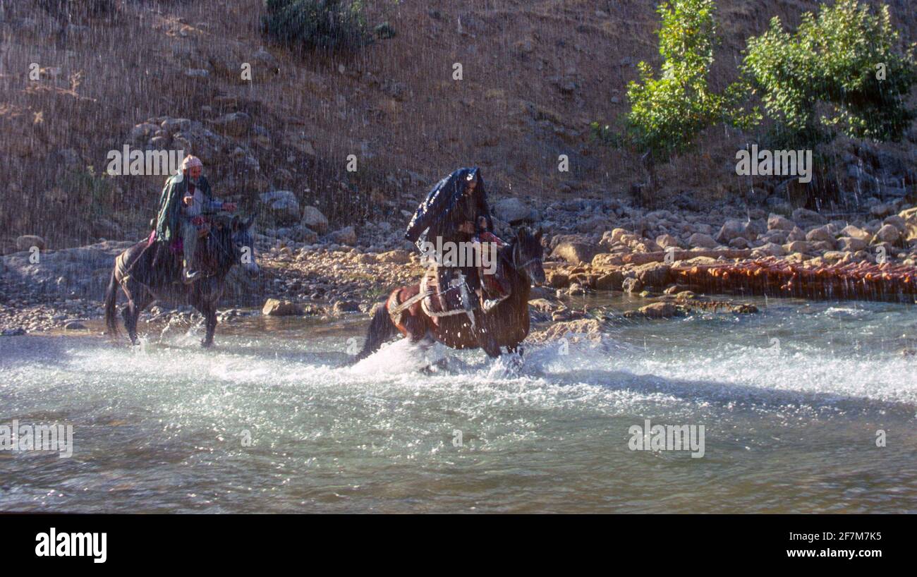 Zwei Reiter reiten durch den schnell fließenden Fluss bei sintflutartigen Regenfällen Zentraltürkei Stockfoto
