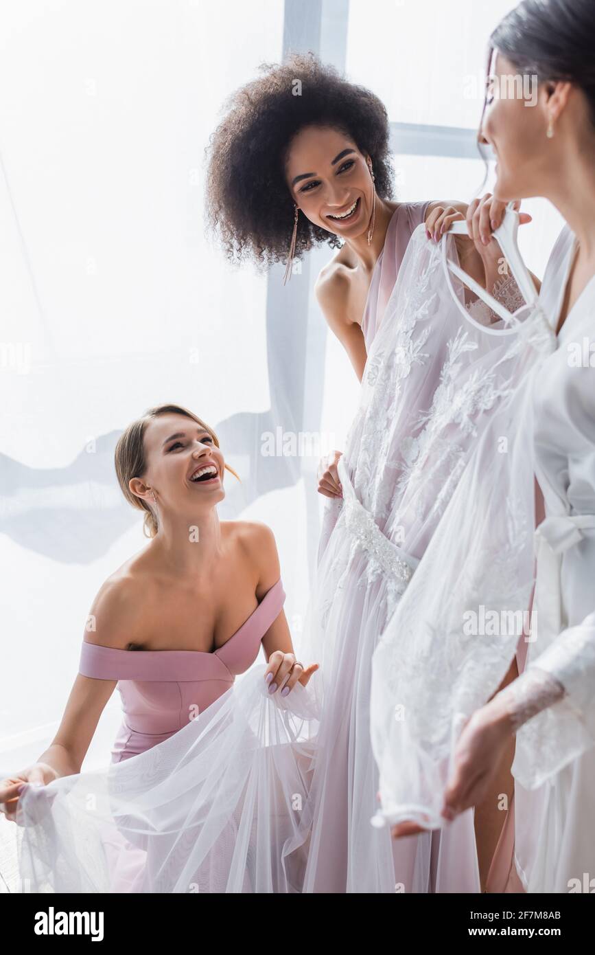 Junge Frau mit weißem Hochzeitskleid in der Nähe aufgeregt multikulturellen Freunden Stockfoto