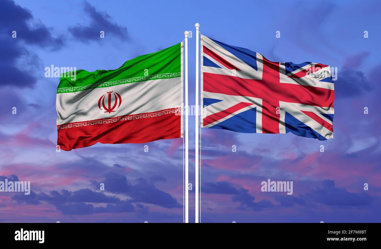 Iran und Großbritannien zwei Flaggen auf Fahnenmasten und blau wolkiger Himmel Stockfoto