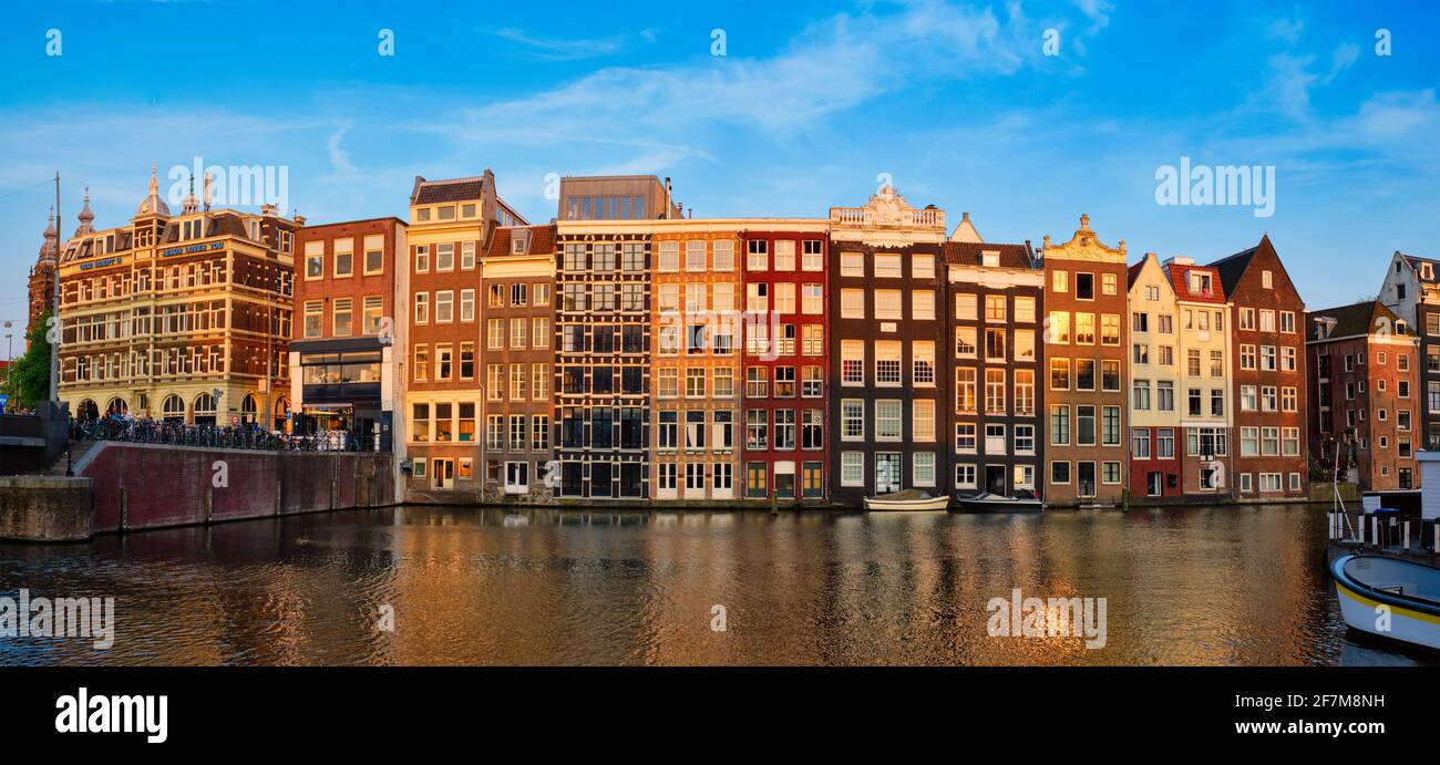 Häuser und Touristenboote auf dem Amsterdamer Grachtenpier Damrak On Sonnenuntergang Stockfoto