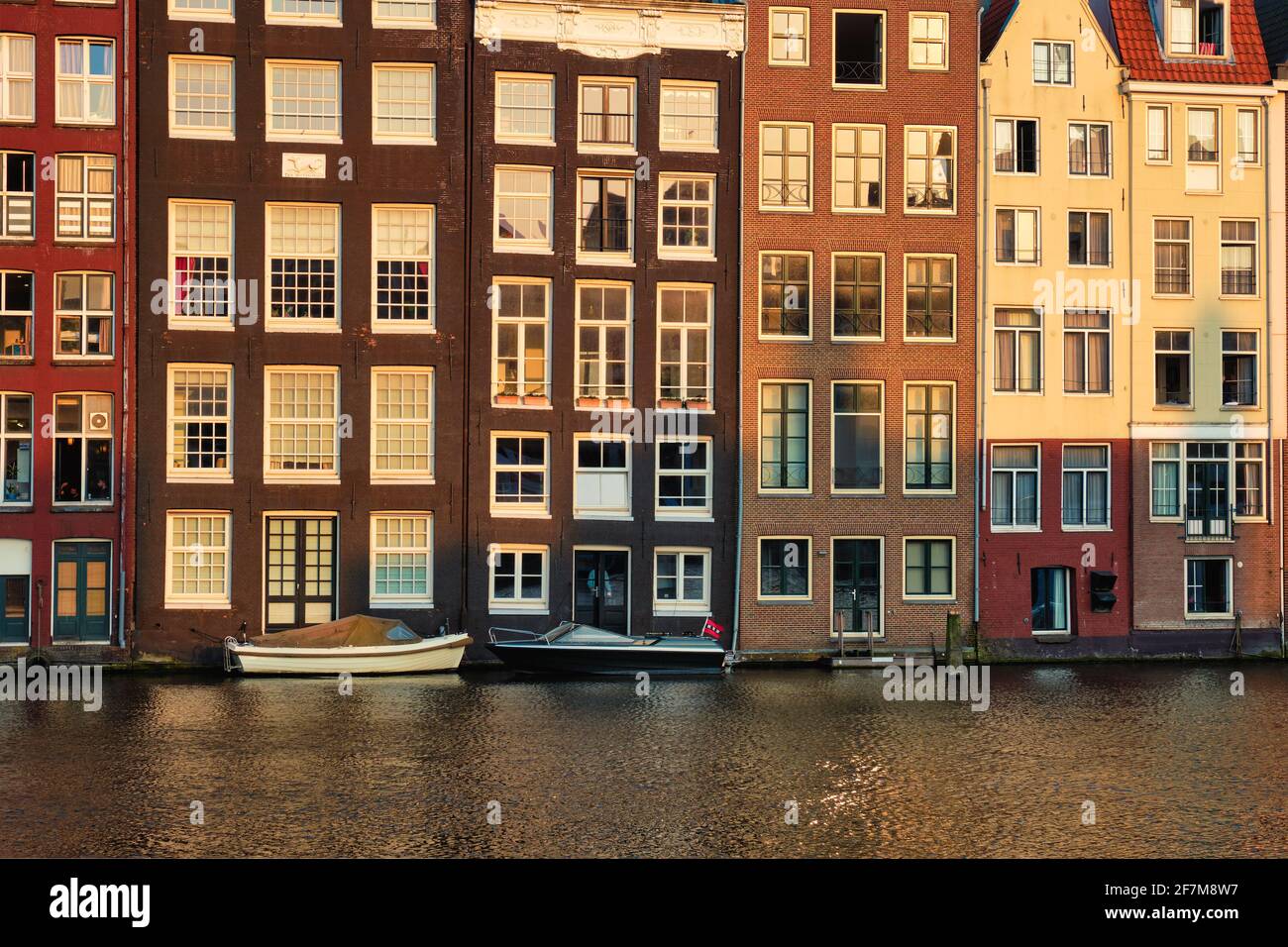Häuser und Boote auf dem Amsterdamer Grachtenpier Damrak bei Sonnenuntergang Stockfoto